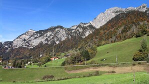 Eine gebirgige Landschaft mit blauem Himmel, einem grünen Tal und einigen Gebäuden in der Ferne.