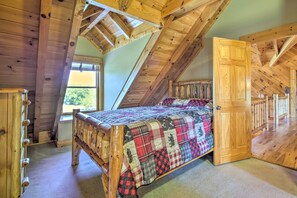 A bedroom with a wooden bed, a window, and a door leading to another room. - Calhoun Cabin w/ River View + Wraparound Deck (Calhoun)