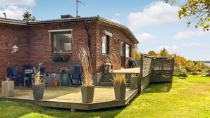 A brick house with a wooden deck, outdoor seating, and a garden.