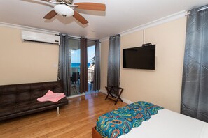Ein Schlafzimmer mit Bett, Sofa, Deckenventilator, Fernseher und Blick ins Freie.