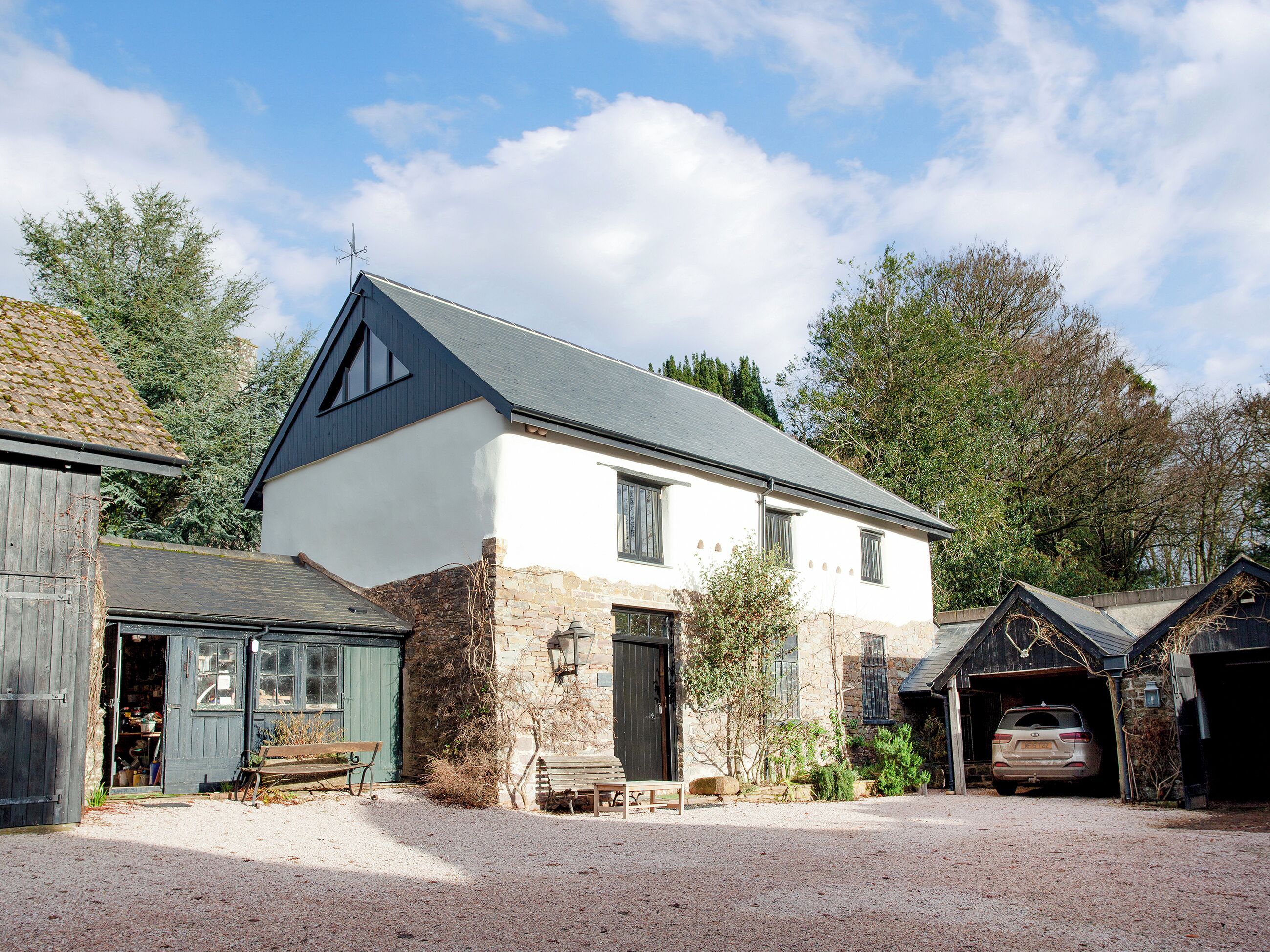 Une maison à deux étages, avec des fondations en pierre, un toit en pente et une allée gravillonnée.