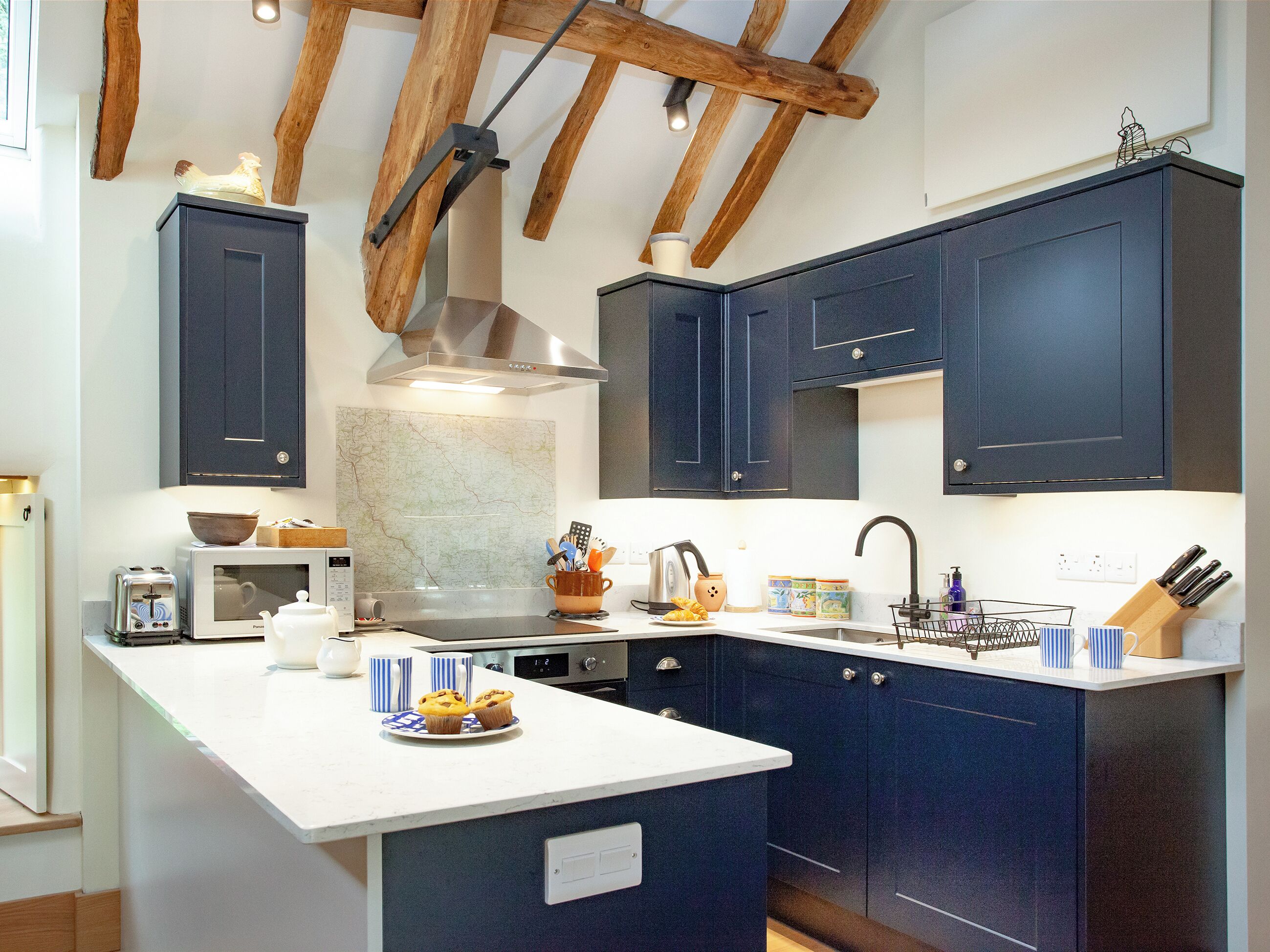 Une cuisine moderne avec des meubles de couleur bleu foncé, un plan de travail blanc, un four encastré et un luminaire suspendu.