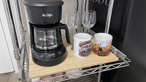 A Mr. Coffee coffee maker on a metal cart with two mugs and two wine glasses.