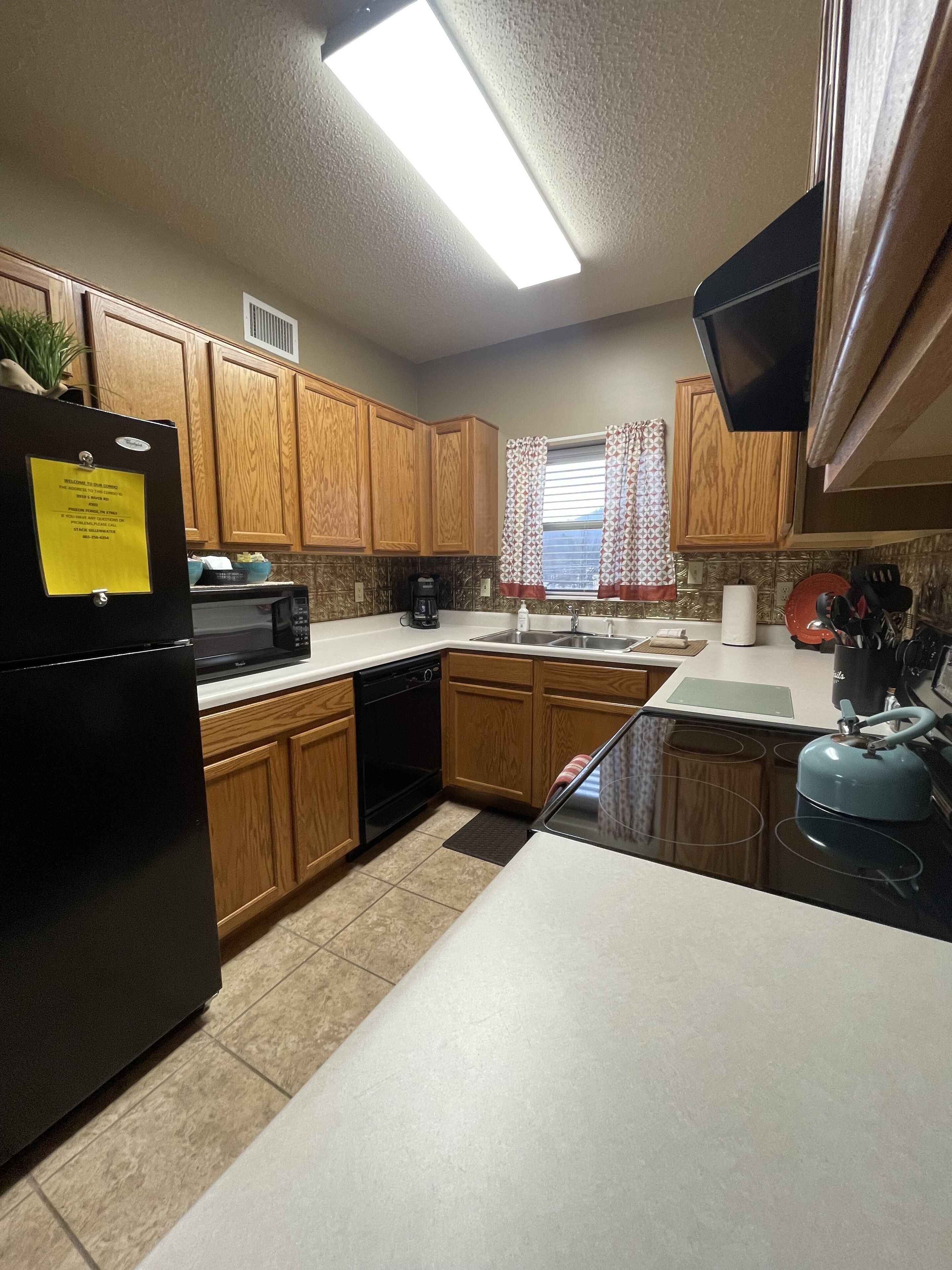 A kitchen with wooden cabinets, a black refrigerator, a microwave, a coffee maker, and a kettle.