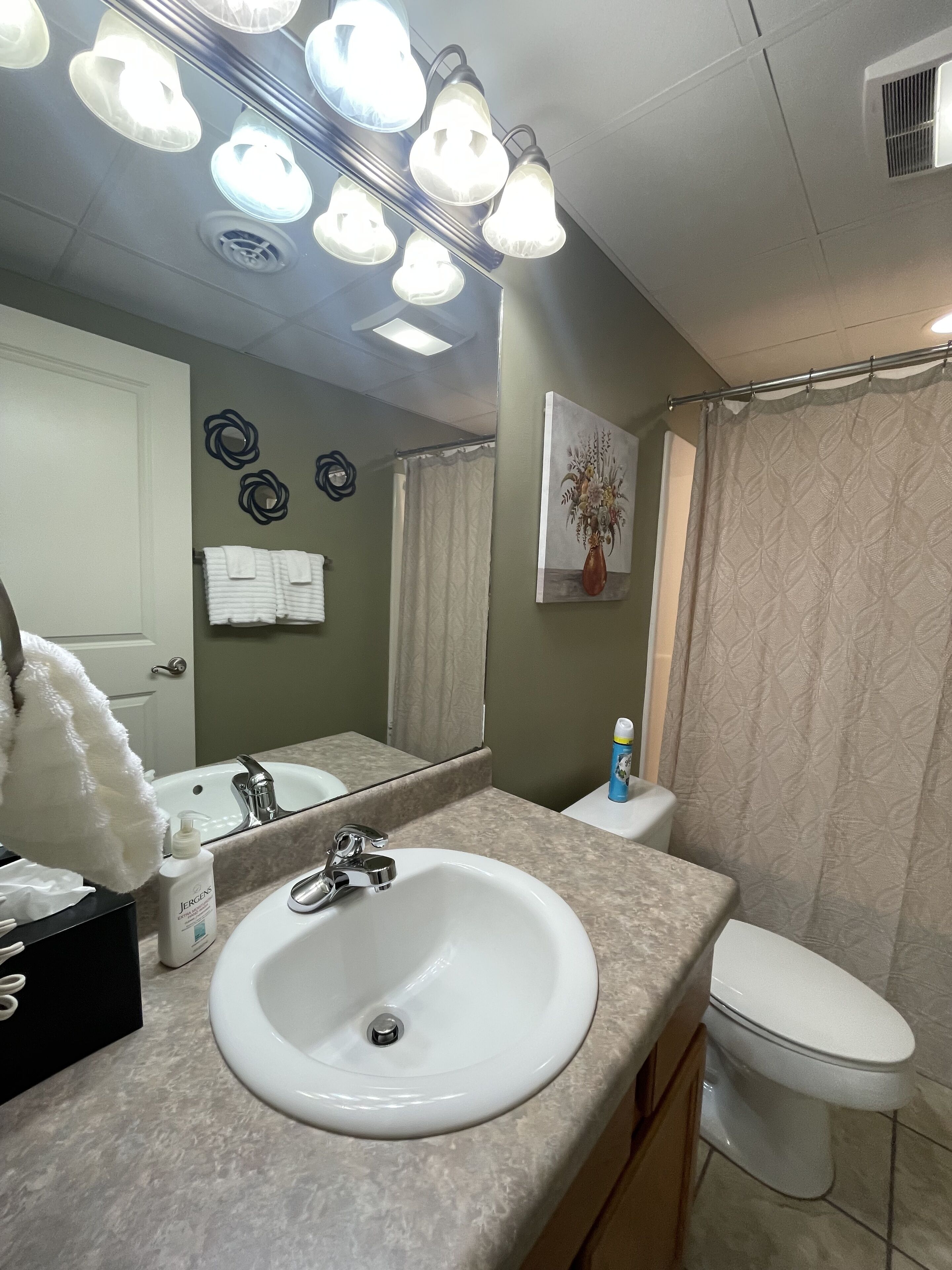 A bathroom with a white sink, mirror, and toilet. There are multiple light fixtures above the mirror.