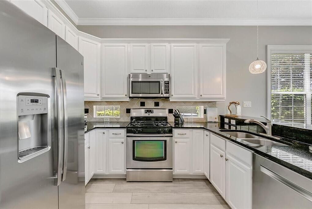 A modern kitchen with white cabinets, stainless steel appliances, and a black countertop.