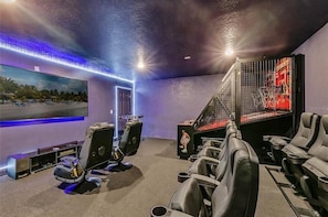 A home theater room with a large screen, reclining chairs, and a staircase leading to a balcony.