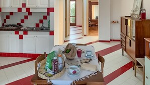 A kitchen with white cabinets and red accents, a dining table with chairs, and a staircase leading to another room.