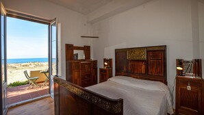A bedroom with a large bed, wooden headboard, and a view of the beach through an open door.