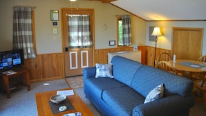 A cozy living room with a blue sofa, wooden ceiling beams, a ceiling fan, and a television on a wooden table. - Bayfield Island View Lodging "Sevona Suite" on Lake Superior with Best Lake view (Bayfield)