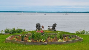 A waterfront garden with raised beds and two Adirondack chairs facing a calm lake with sailboats. - Bayfield Island View Lodging "Sevona Suite" on Lake Superior with Best Lake view (Bayfield)