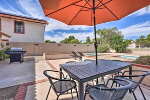 Un patio con mesa y sillas, una parrilla y una piscina.