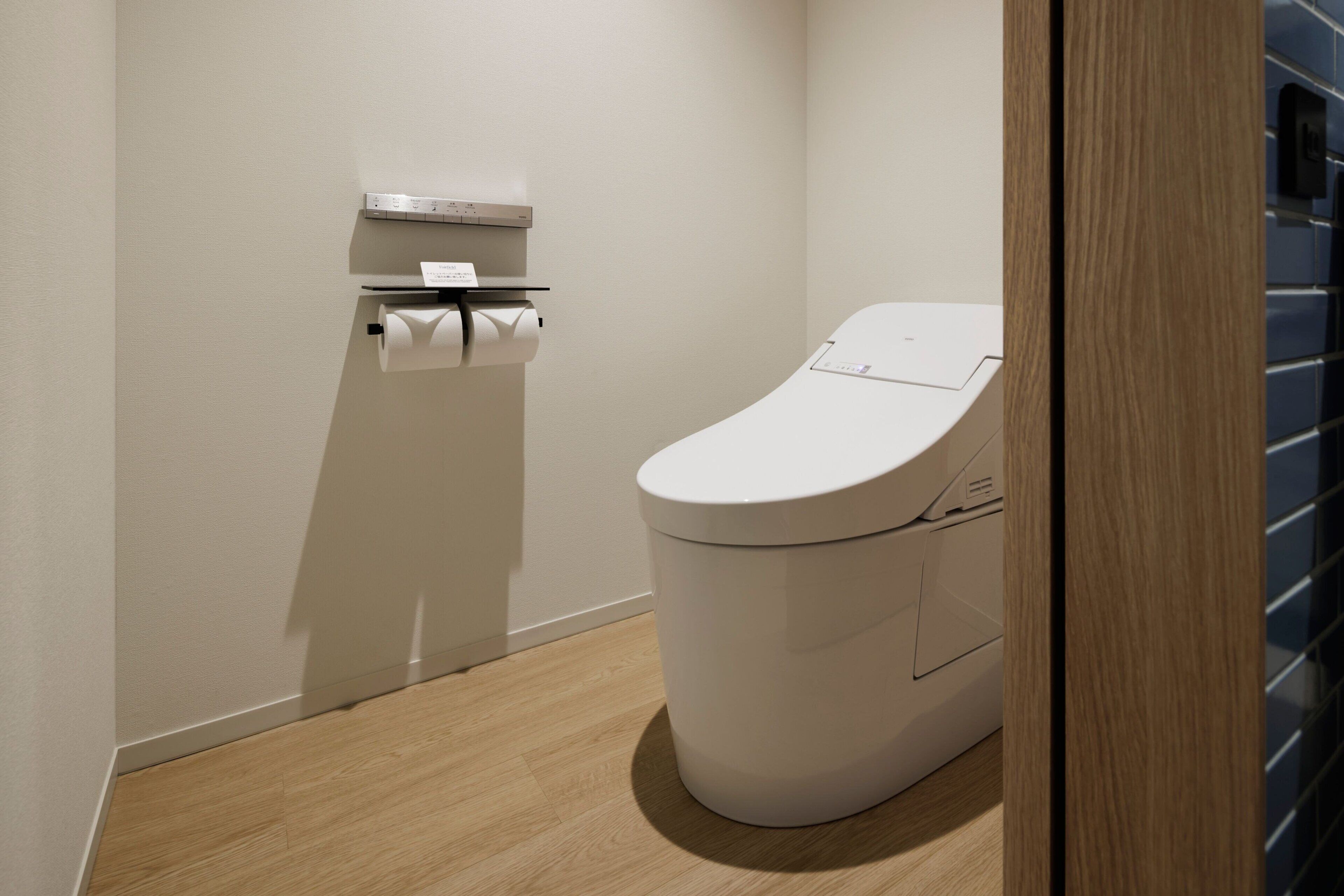 A modern bathroom with a toilet, a paper towel dispenser, and a toilet paper roll on the wall.