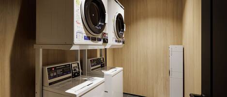 A laundry room with two front-loading washing machines and a dryer, wooden walls, and a tiled floor.