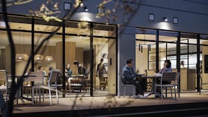 Un área de estar al aire libre con mesas y sillas, puertas de vidrio que dan a un espacio interior e iluminación colgante.