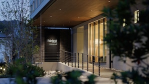 Una entrada de hotel moderna con una escalera que lleva al vestíbulo, rodeada de vegetación.