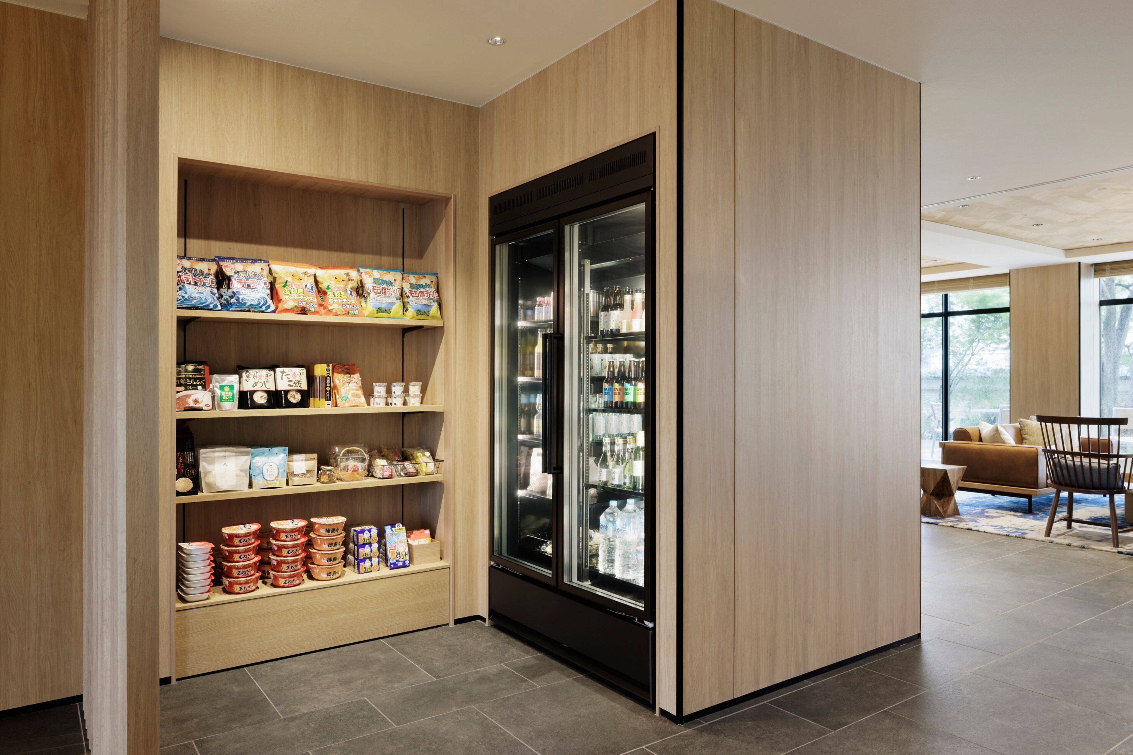 A modern interior with a wooden shelving unit displaying various food items and a black refrigerator.