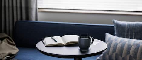 Una mesa redonda con un libro y una taza sobre un sofá azul.