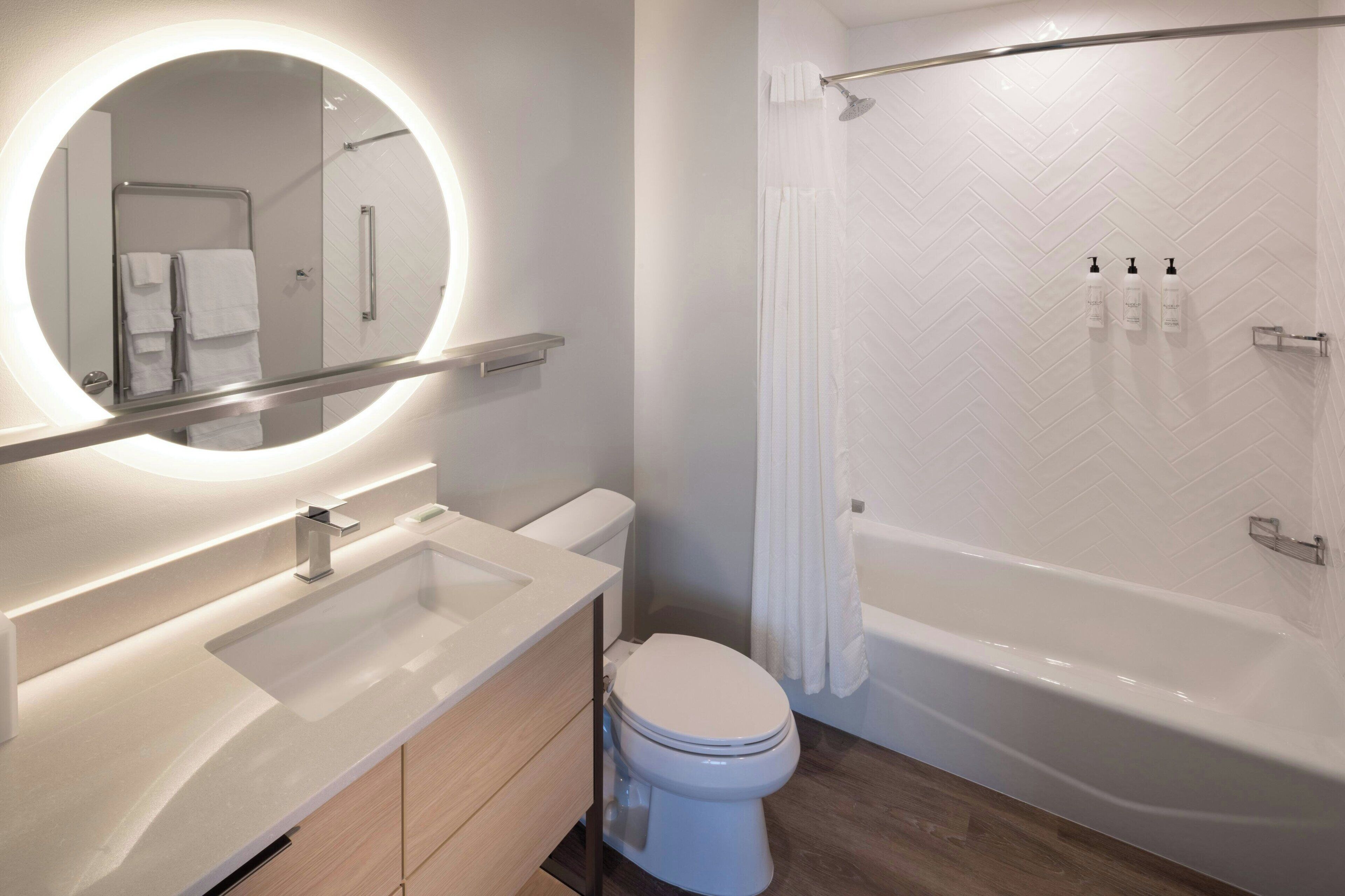 A modern bathroom with a round mirror, a sink, a toilet, and a bathtub.