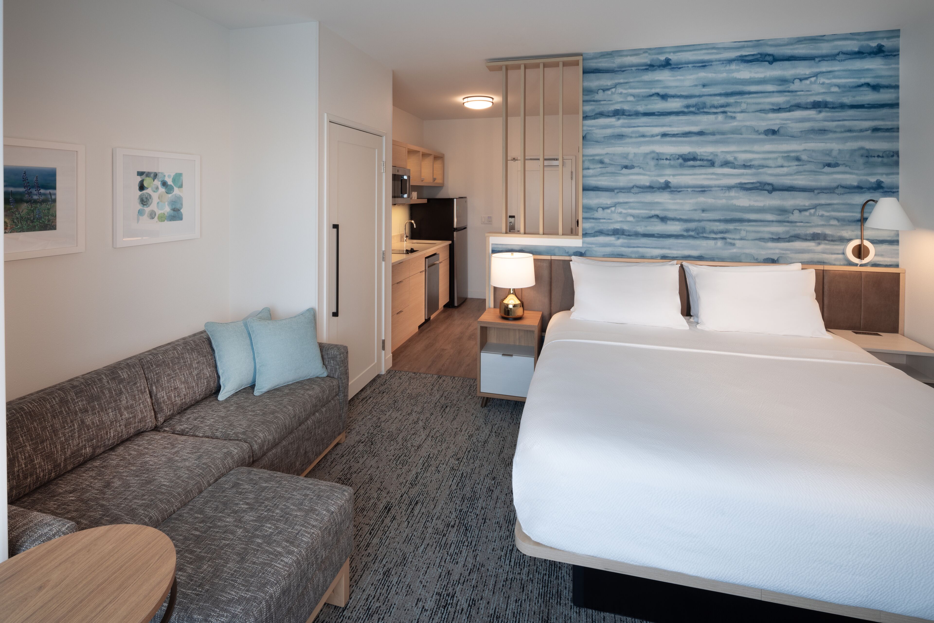 Ett modernt hotellrum med en stor säng, en soffa, en liten köksdel och utsikt över havet.