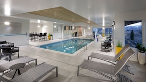 Een modern binnenzwembad met loungebedden, een zwembad en uitzicht op een besneeerd landschap.