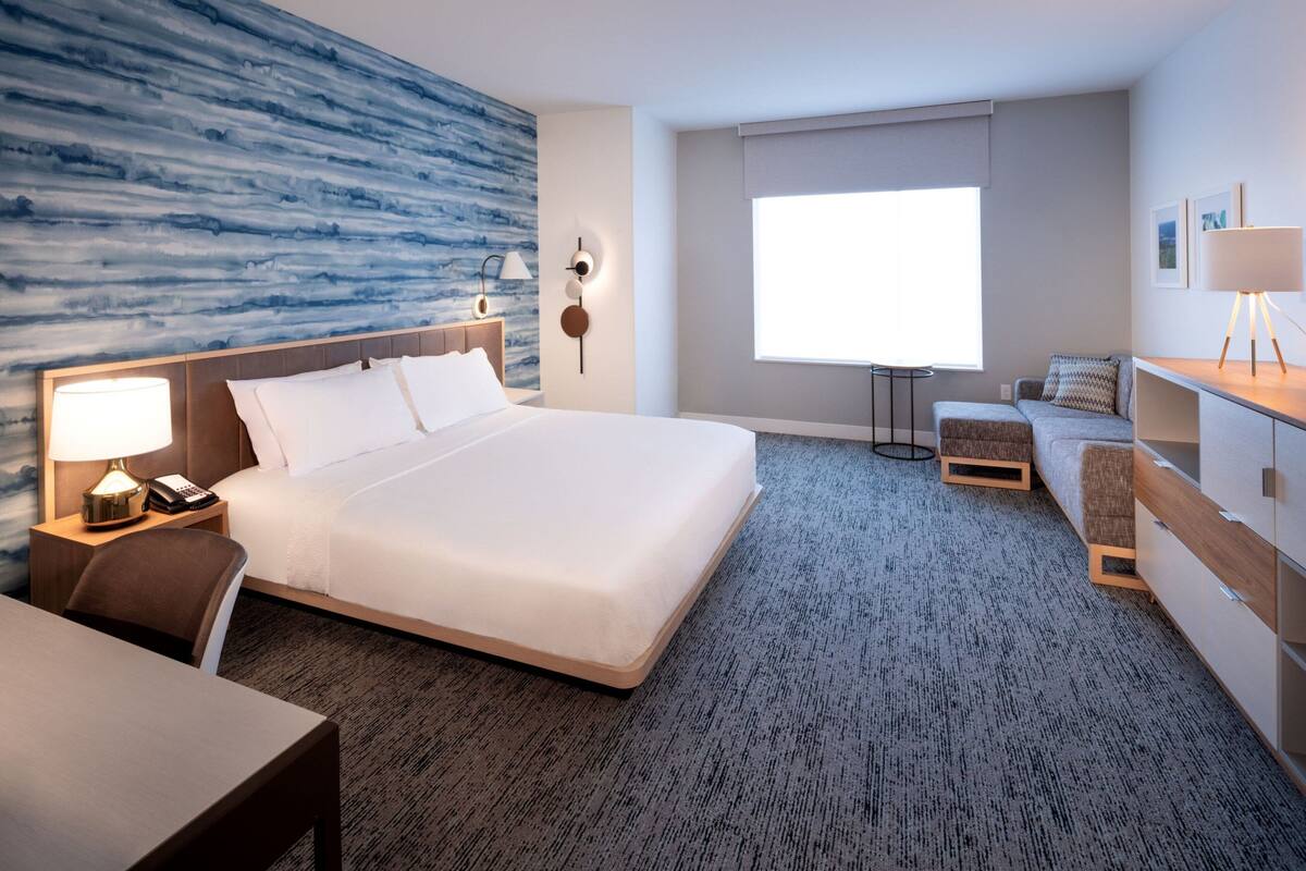 Una habitación de hotel con una cama grande, un escritorio, una silla, un sofá, una lámpara, una mesita de noche y una ventana con vistas.
