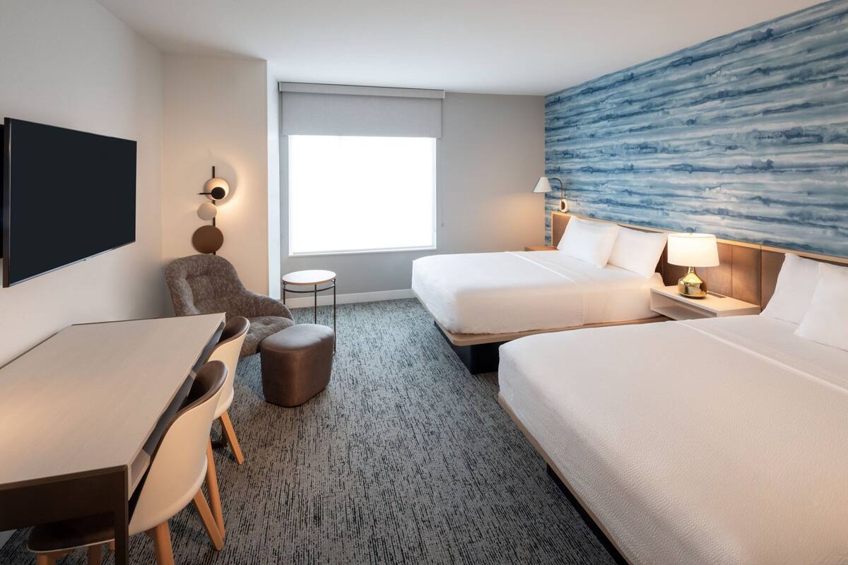 Una habitación de hotel con una cama, un escritorio, una silla, una mesa redonda pequeña y un televisor instalado en la pared.