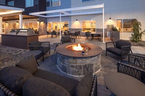 Un espace extérieur aménagé en patio, avec un foyer en pierre, des coins salon et une partie couverte comprenant des tables et des chaises.
