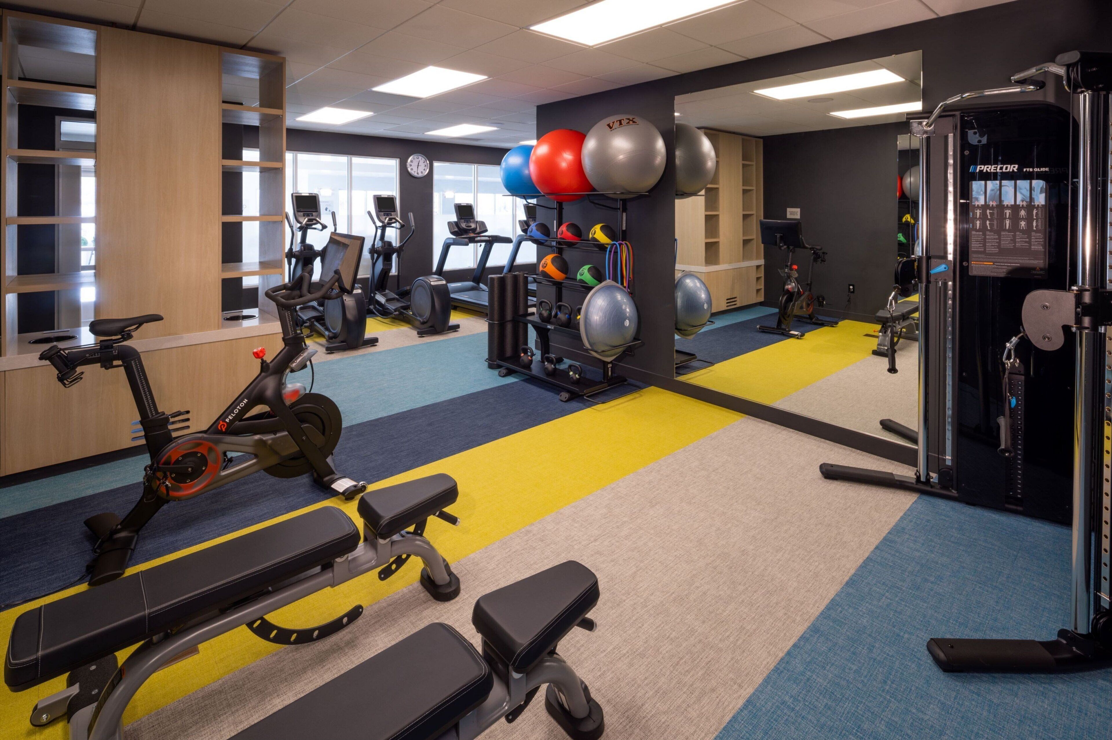 Un gimnasio con equipamiento de ejercicio, bancos y un espejo grande.
