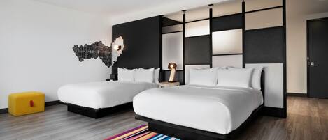 A modern hotel room with two beds, a colorful striped rug, a unique wall art piece, and a small yellow ottoman.