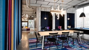Un espace repas moderne avec une longue table, des chaises noires et un tapis rayé aux couleurs vives.