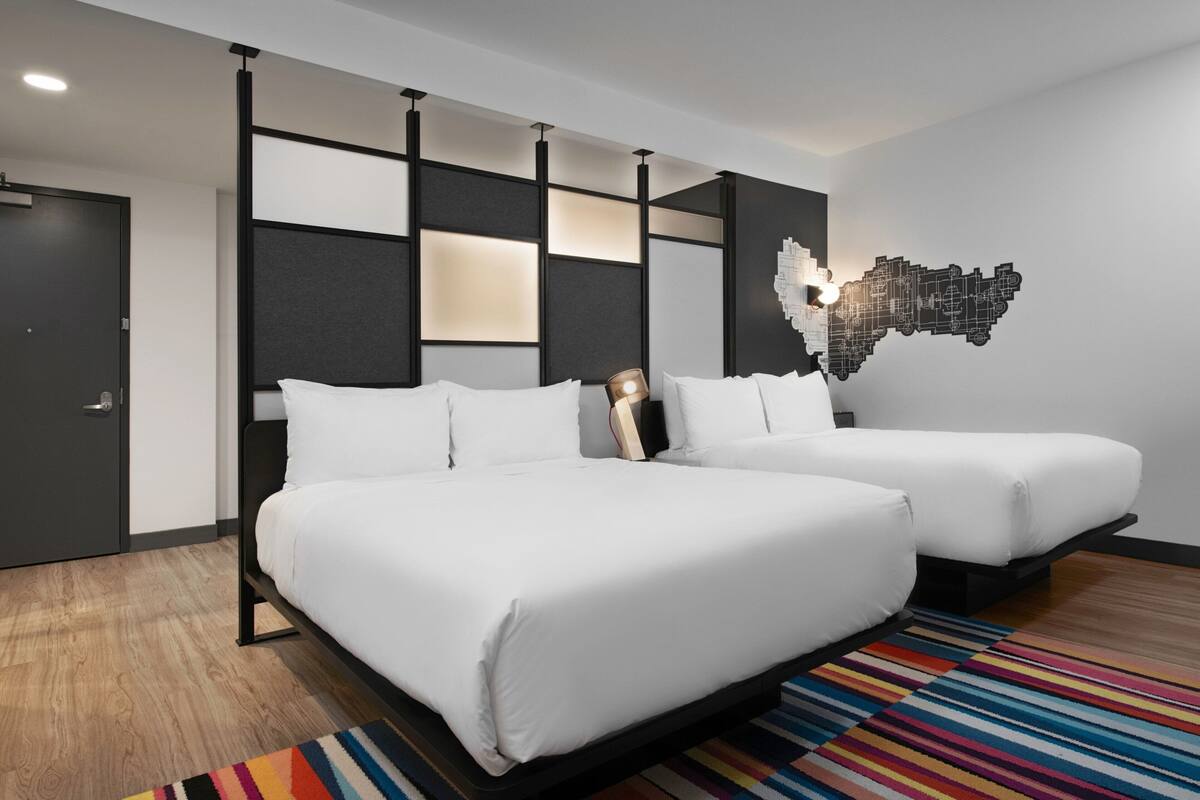 Una habitación de hotel moderna con dos camas, un tapete a rayas de colores y una obra de arte en la pared.