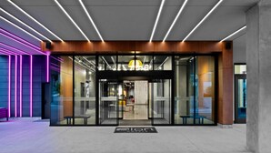 Une entrée d’hôtel moderne avec des portes en verre, un comptoir d’accueil et une enseigne lumineuse au néon.