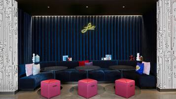 A modern lounge area with a dark blue sofa, pink ottomans, and a neon sign.