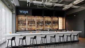 Un espace bar doté d’un comptoir blanc, de tabourets de bar noirs et d’étagères remplies de bouteilles.