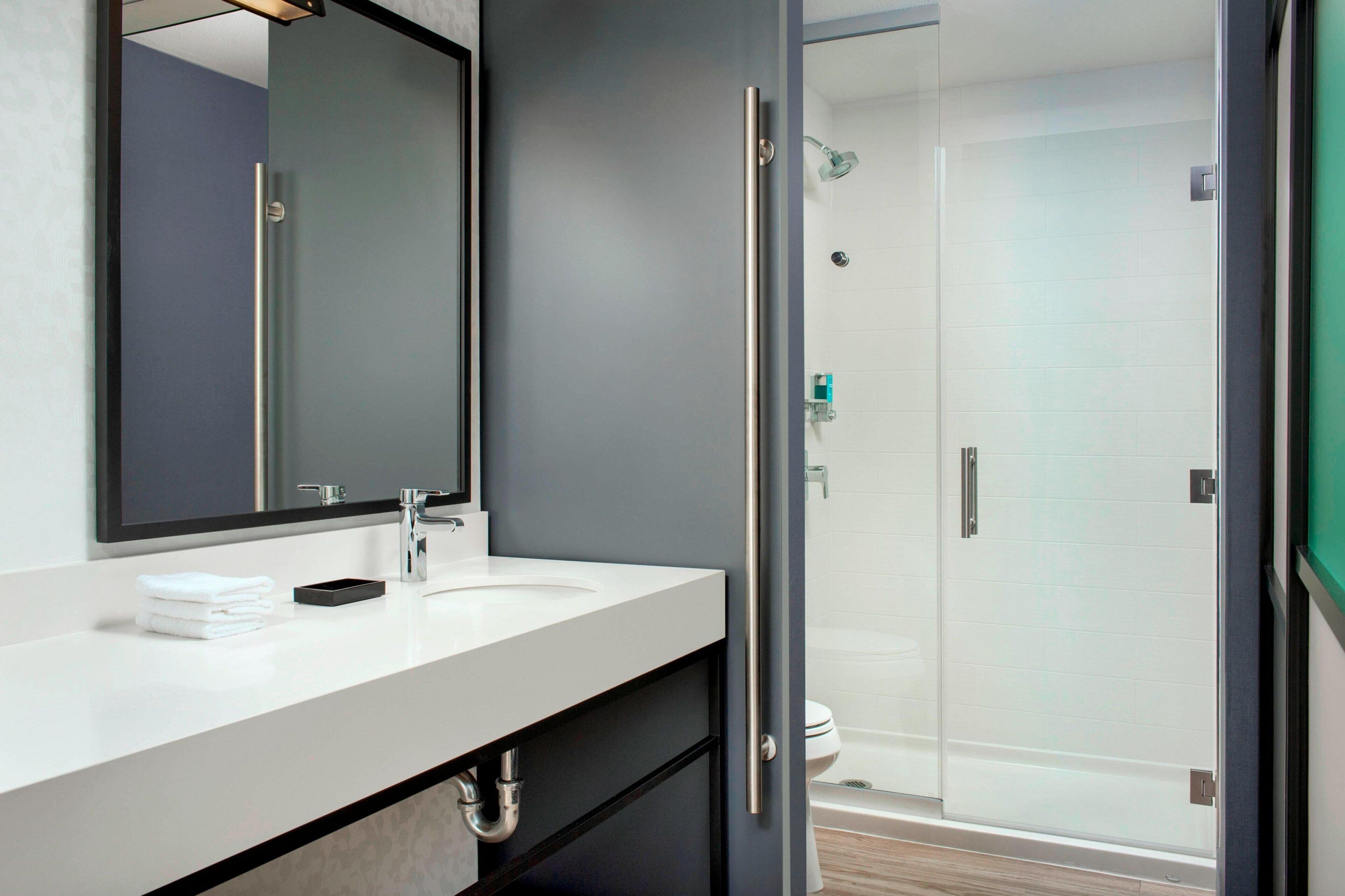 Un bagno moderno con un lavandino bianco, un ampio specchio e un box doccia in vetro.