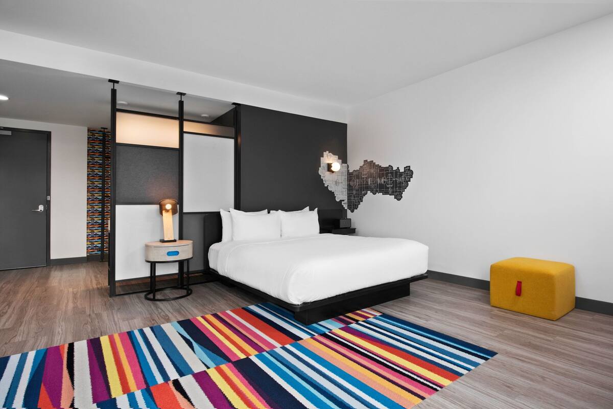Un dormitorio moderno con una cama, una mesita de noche, una lámpara, una alfombra colorida y una original obra de arte en la pared.