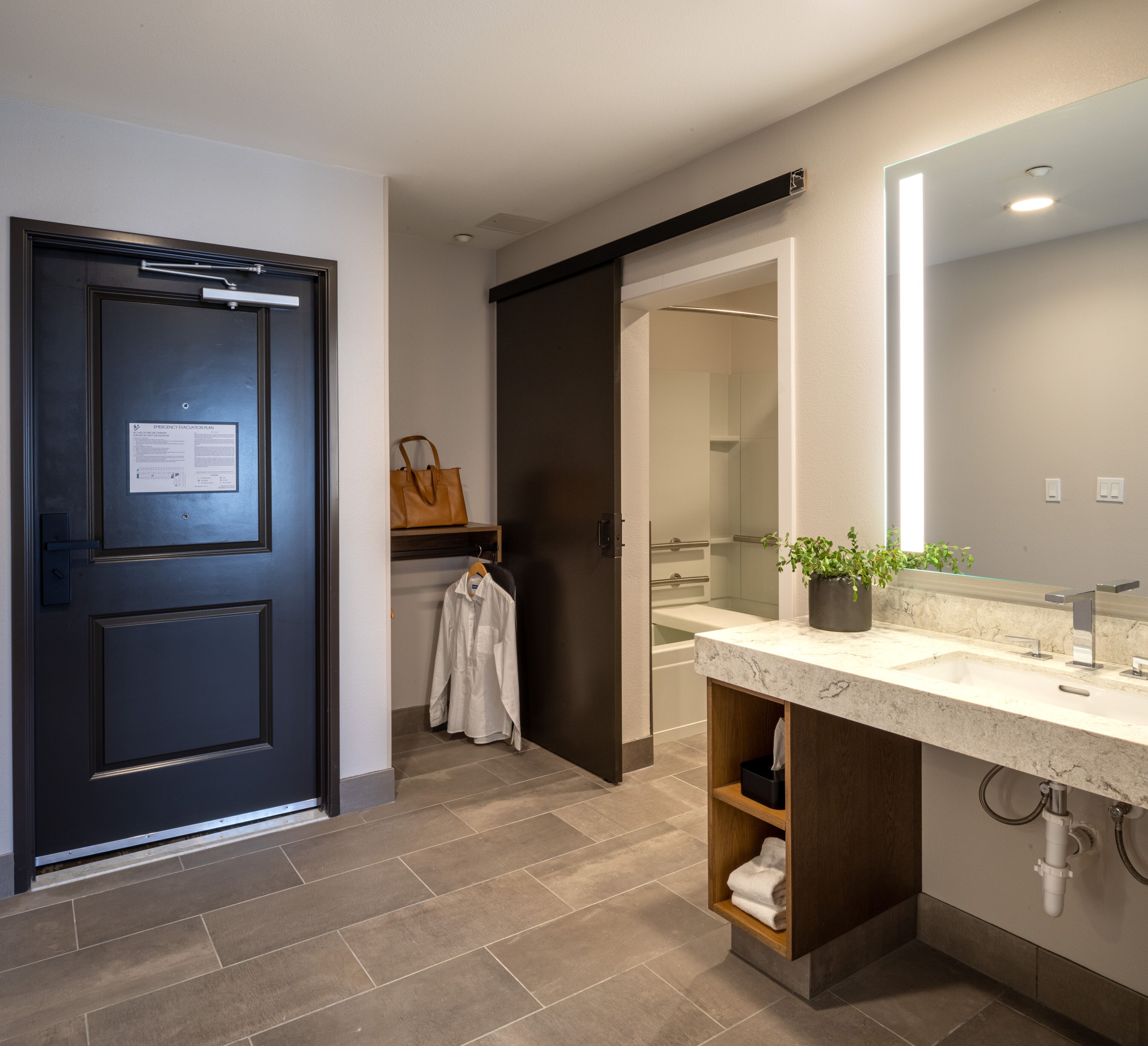 A modern bathroom with a dark door, a white sink with a marble countertop, a mirror, and a towel rack.