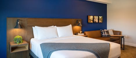 Ein Hotelzimmer mit einem großen Bett, einem Holzkopfende, zwei Nachttischen mit Lampen, einer blauen Wand und einer kleinen Pflanze.