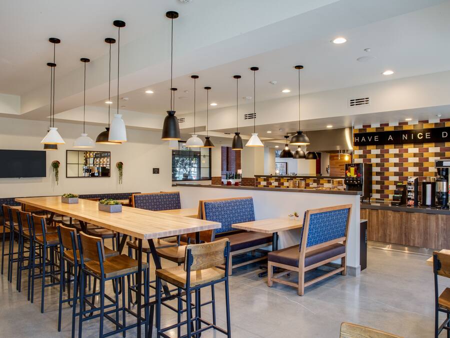 A modern restaurant with a long communal table, booths, and hanging pendant lights.
