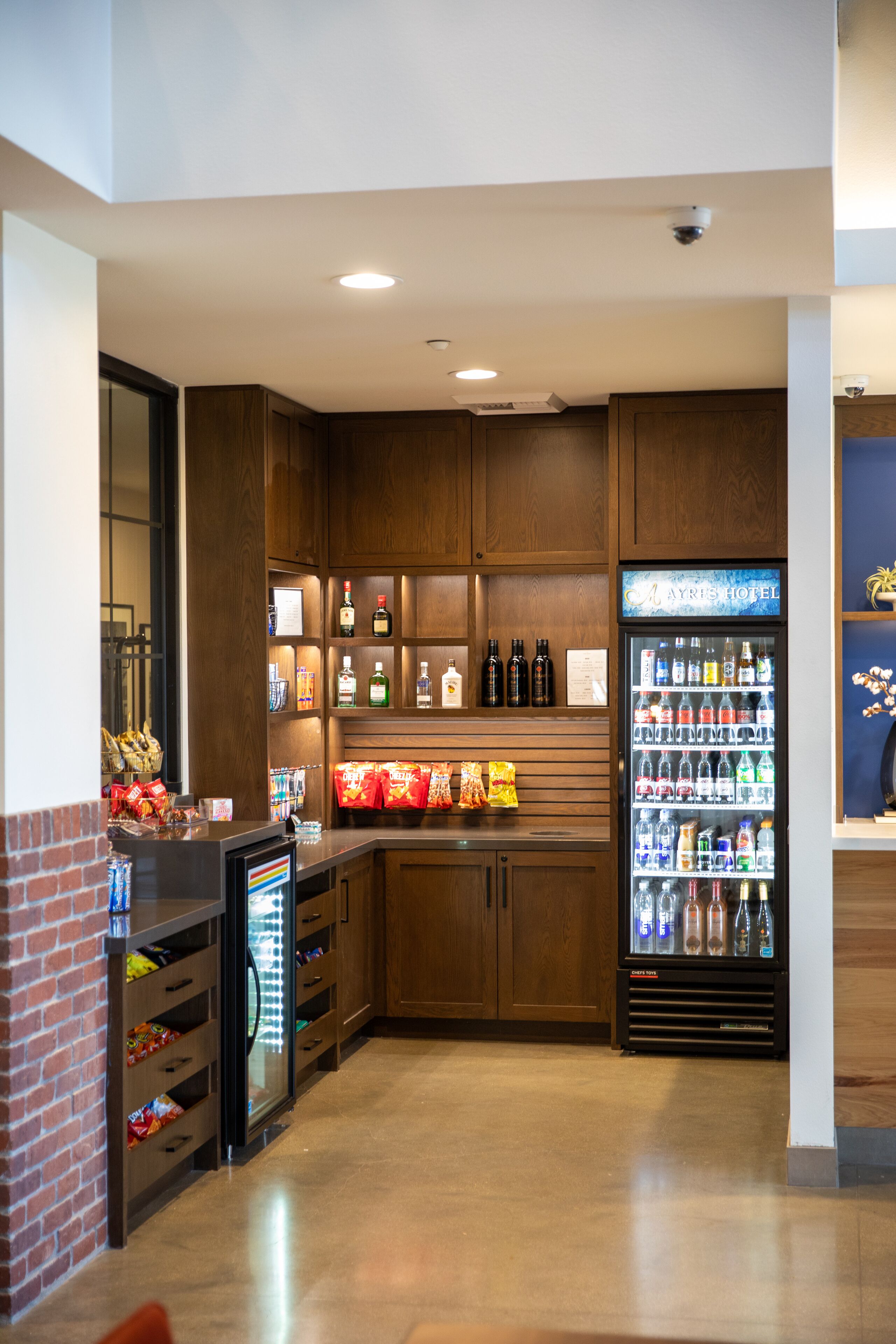 A hotel bar area with wooden cabinets, a minibar, and a beverage refrigerator.