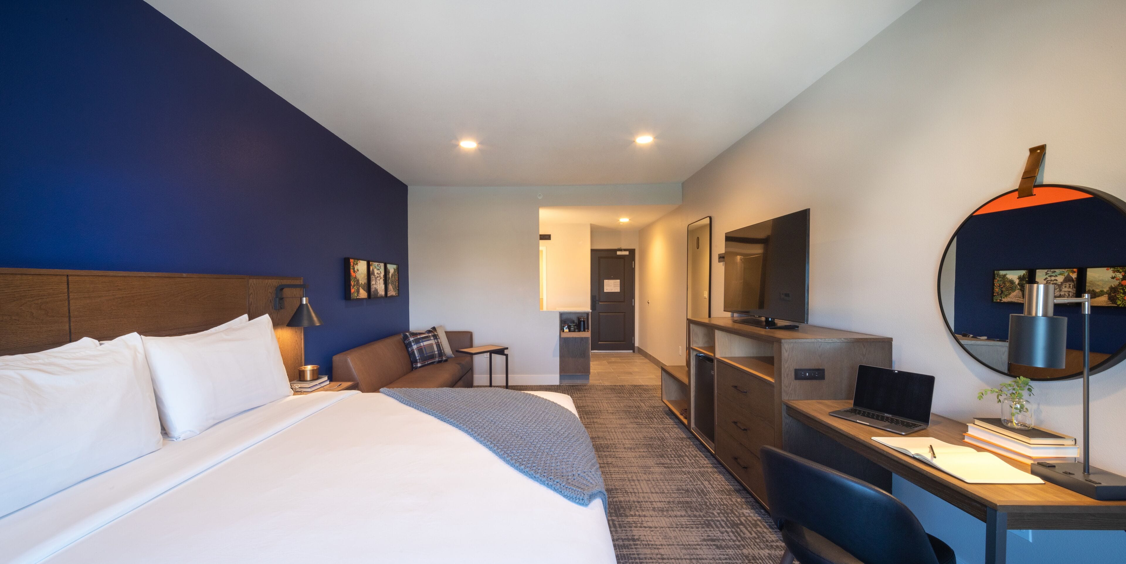 Una habitación de hotel con una cama grande, un escritorio con una computadora portátil, un espejo y un televisor.