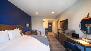 Una habitación de hotel con una cama grande, un escritorio con una computadora portátil, un espejo y un televisor.