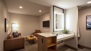 A modern hotel room with a sofa, a small table, a wooden cabinet, a bathroom with a sink and mirror, and a TV mounted on the wall. - Ayres Hotel Rialto Fontana (Rialto)