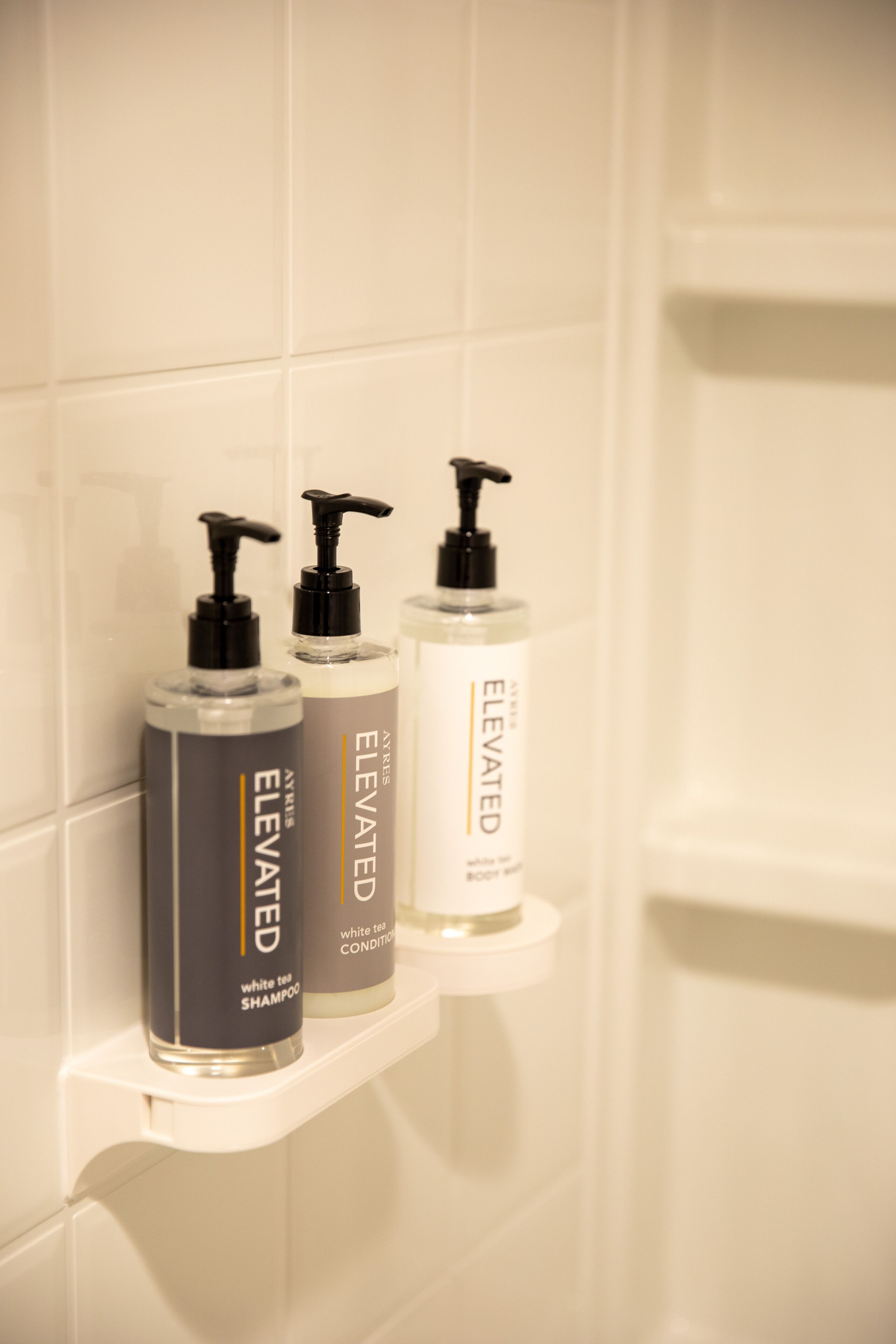 Three bottles of body wash on a white shelf in a bathroom.
