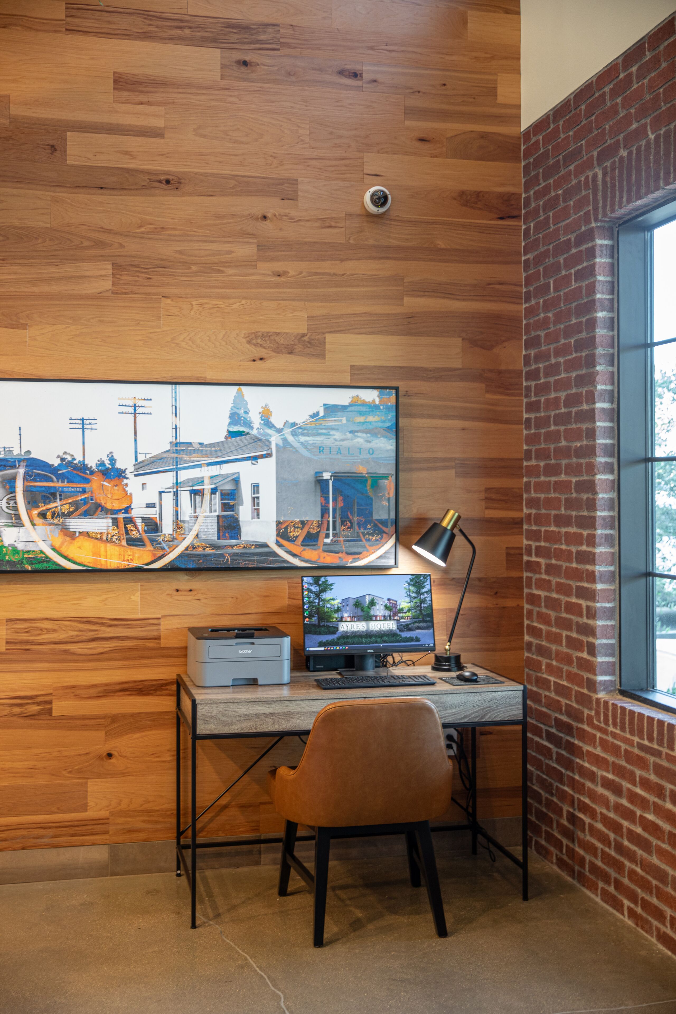 A wooden desk with a computer, a chair, and a framed picture on the wall.