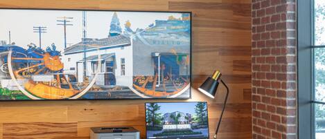 A wooden desk with a computer, a chair, and a framed picture on the wall.