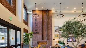 A modern lobby with a brick wall, a fireplace, seating areas, and a large plant. - Ayres Hotel Rialto Fontana (Rialto)