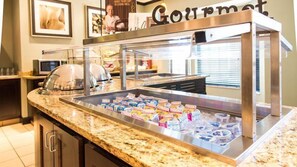 A buffet area with a marble countertop, a glass display case with food items, and a sign that reads 'Gourmet.' - 1 Bedroom | Free Breakfast (Fargo)