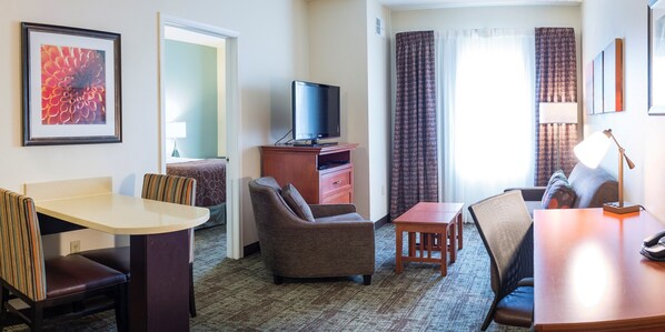 A hotel room with a television, a dining table, a sofa, and a small wooden table. - 1 Bedroom | Free Breakfast (Fargo)